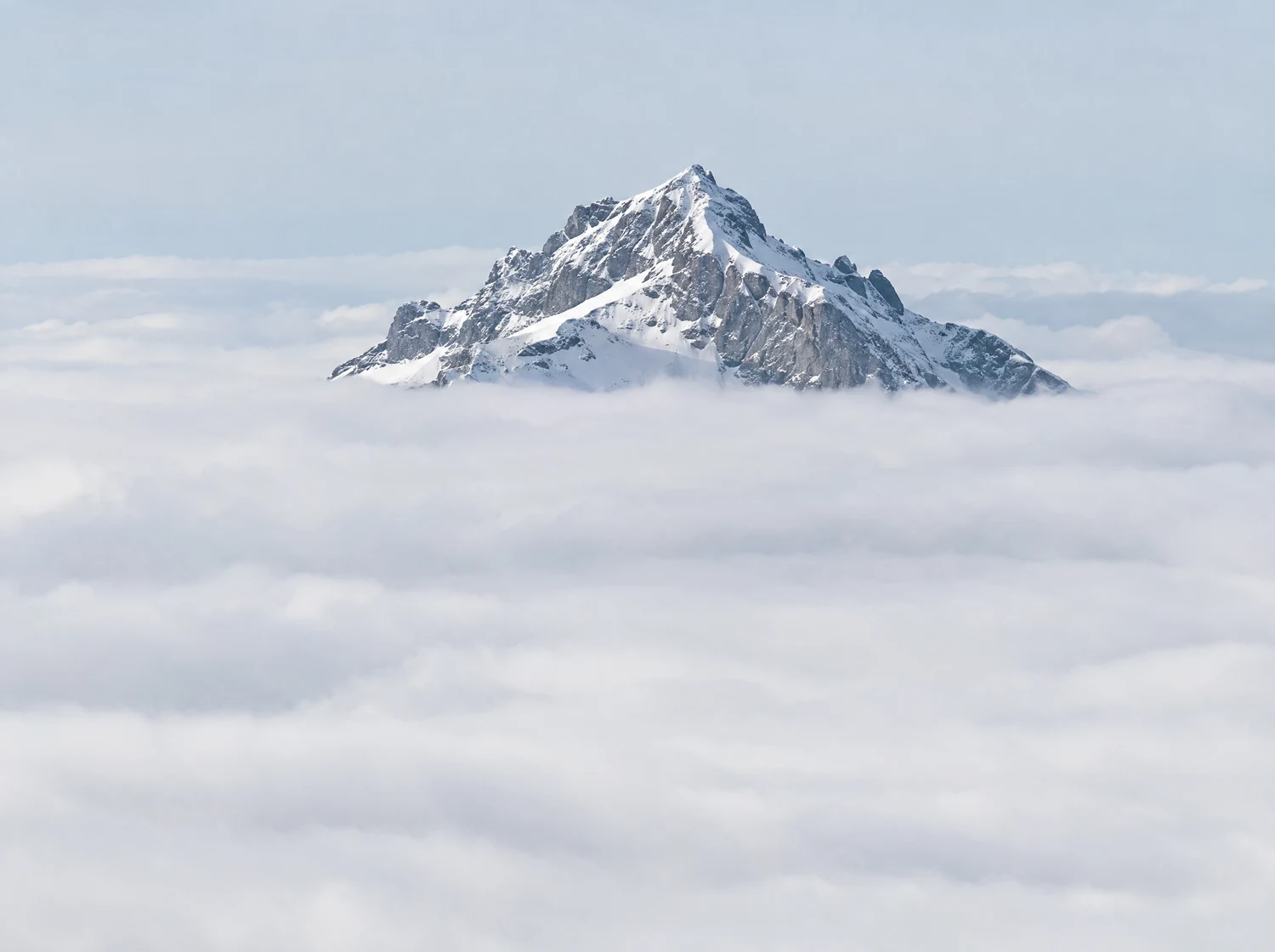 A snow-capped alpine summit above low winter cloud